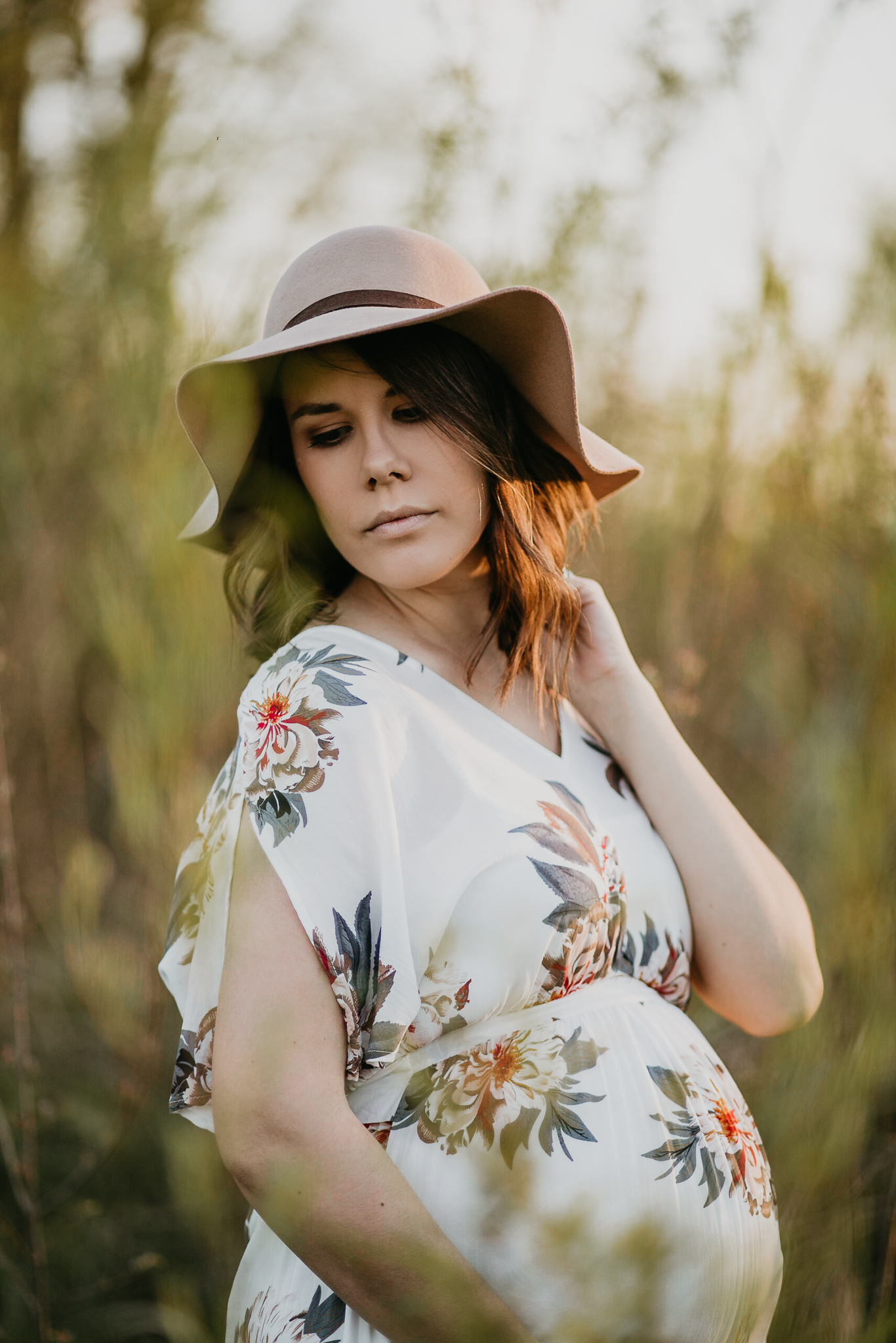 Expecting woman in a sun hat in a golden field of grasses.